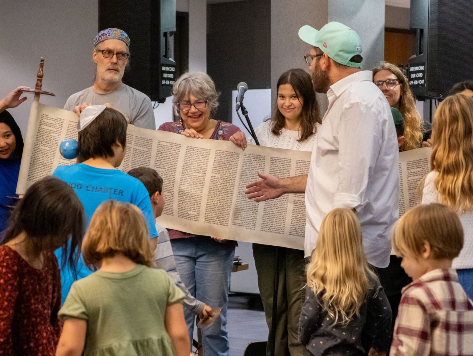 Congregants hold up an open Torah scroll while a Rabbi points to the text and reads