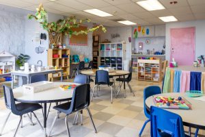 Inside of a preschool classroom. The colorful room is filled with child-sized tables and shelves, toys, and books.