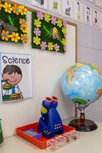 A kid's microscope and globe sit on a table in a preschool classroom