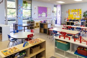 Inside of a preschool classroom. The colorful room is filled with child-sized tables and shelves, toys, and books.