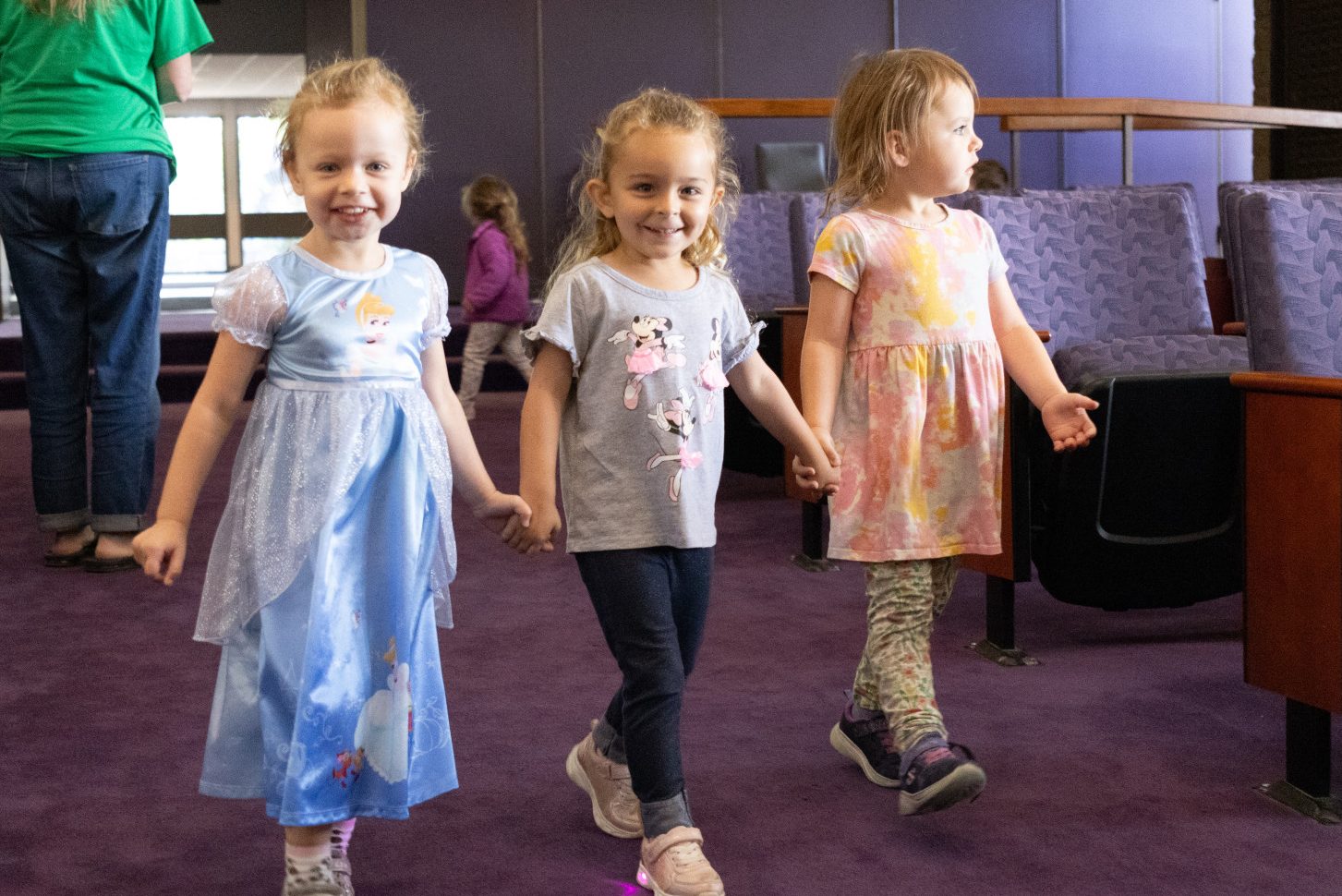 Three preschool girls walk together holding hands