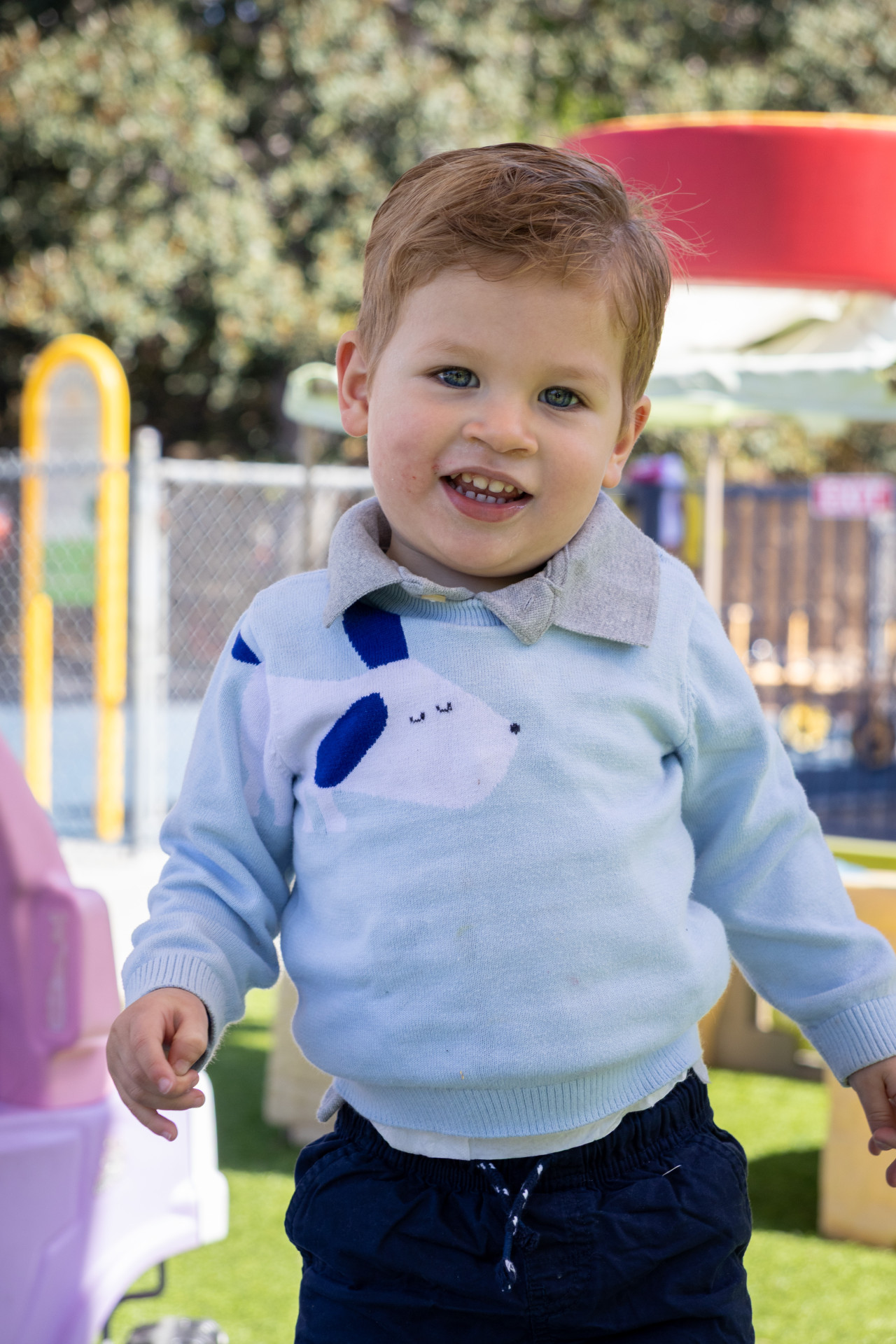 A toddler smiles on the playground at Silverman Preschool