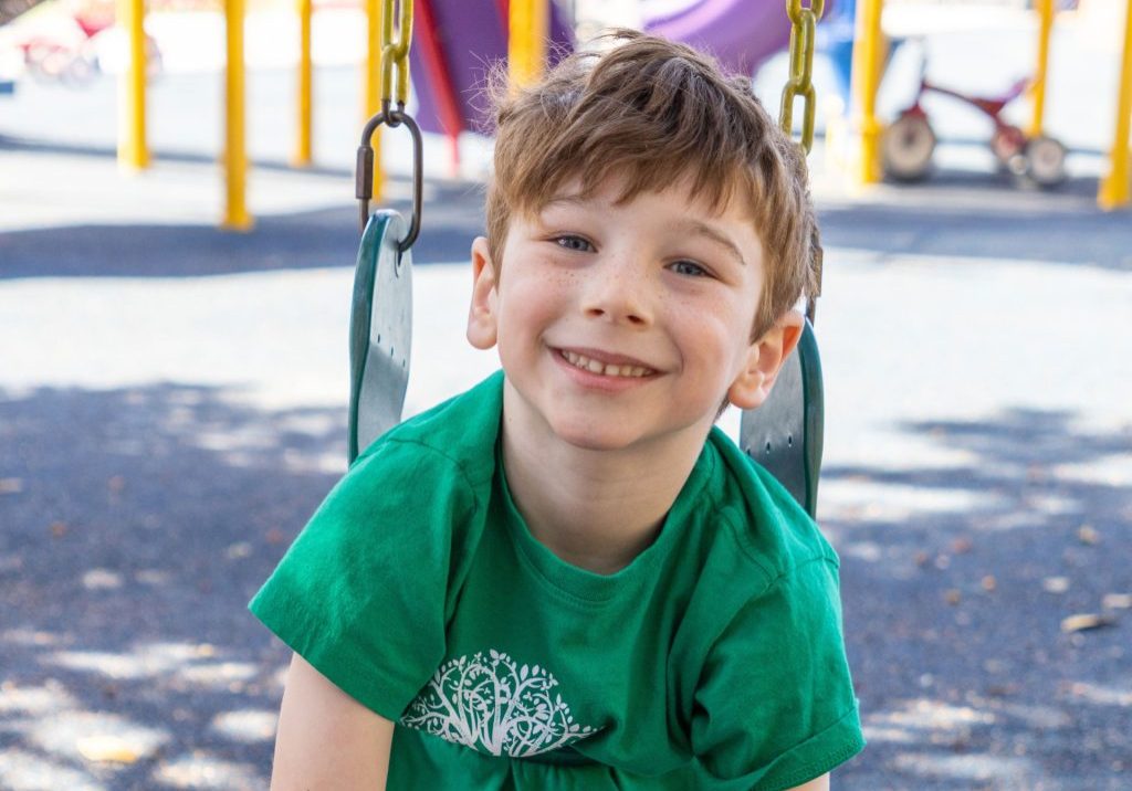 A preschool boy hanging on a swing.